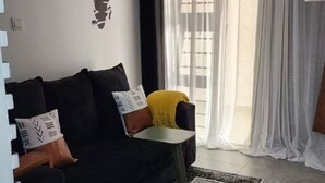 Ein modernes Wohnzimmer mit einer schwarzen Couch, einem kleinen Beistelltisch und transparenten Vorhängen.