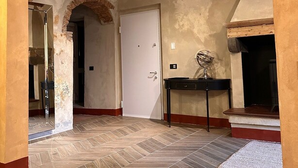 Una habitación amplia con suelo de madera en patrón de espiga, arcos de ladrillo visto y chimenea.