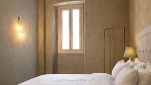 Un dormitorio con cama, mesita de noche, lámpara y ventana.