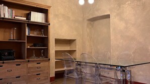 Un comedor con una mesa de vidrio, sillas transparentes, una estantería y una lámpara en el techo.