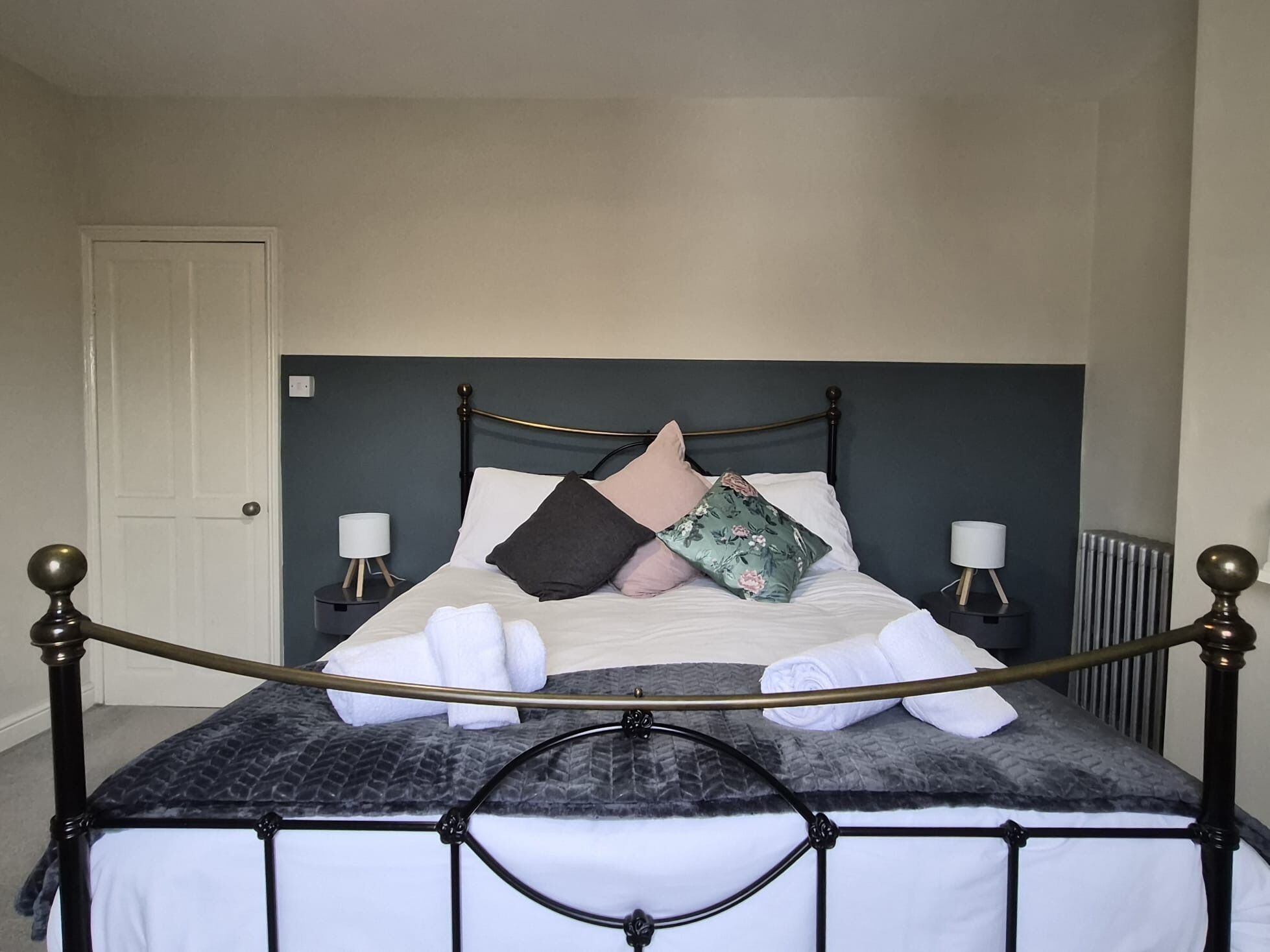 A neatly made bed with a headboard, two bedside tables with lamps, and a radiator.