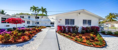 A row of white mobile homes with colorful flower beds in front, a clear sky, and a palm tree.