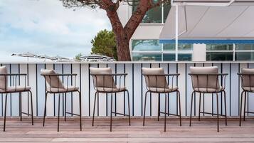 A row of outdoor bar-style chairs with metal frames and cushioned seats, aligned against a white wall with vertical lines.