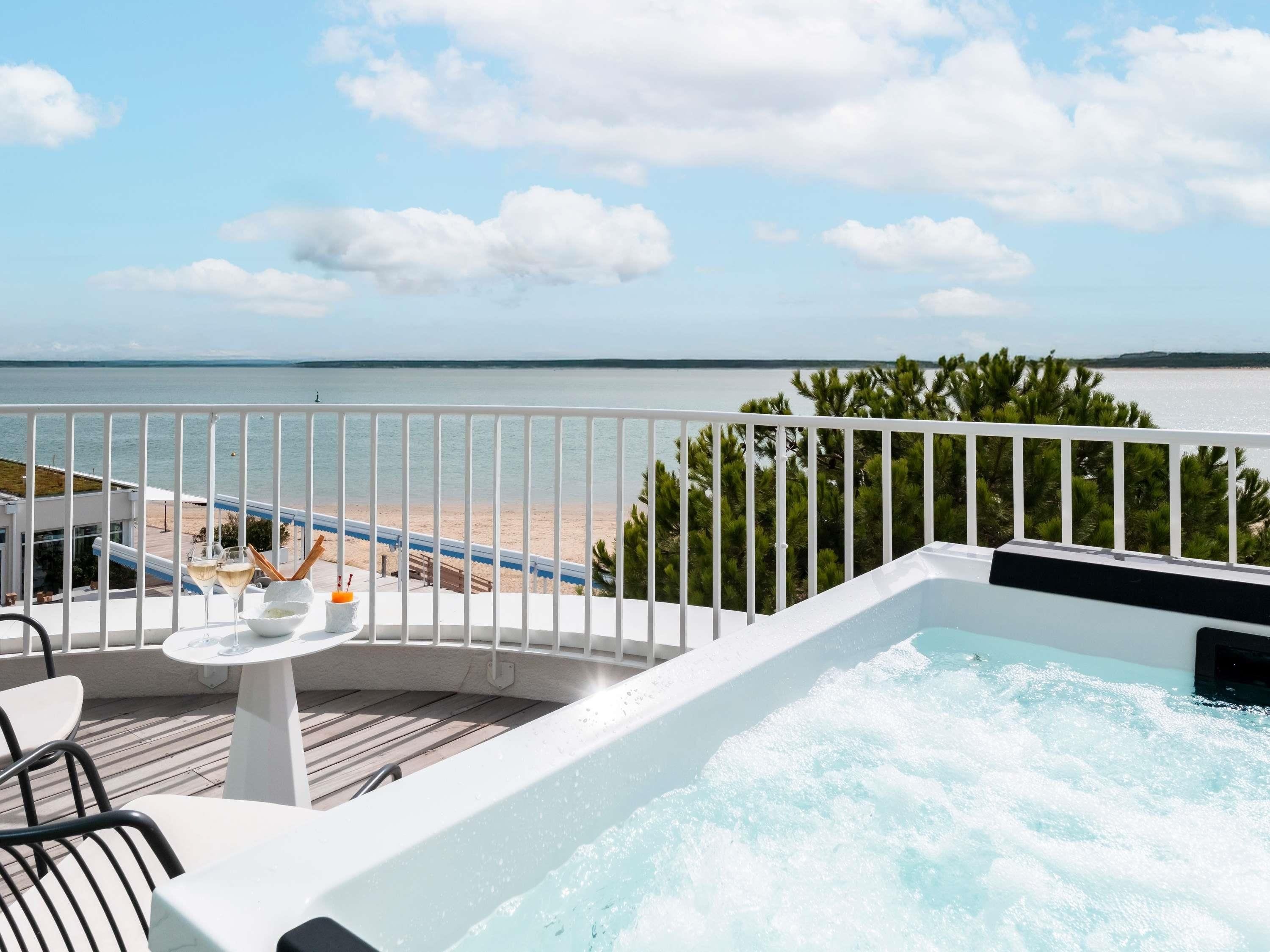 Un balcon avec un jacuzzi, une table avec des boissons et une vue sur la plage et l’océan.