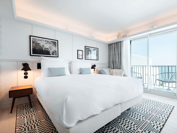 Ein modernes Hotelzimmer mit einem großen Bett, einem kleinen Beistelltisch, einem Nachttisch und einem Balkon mit Blick.