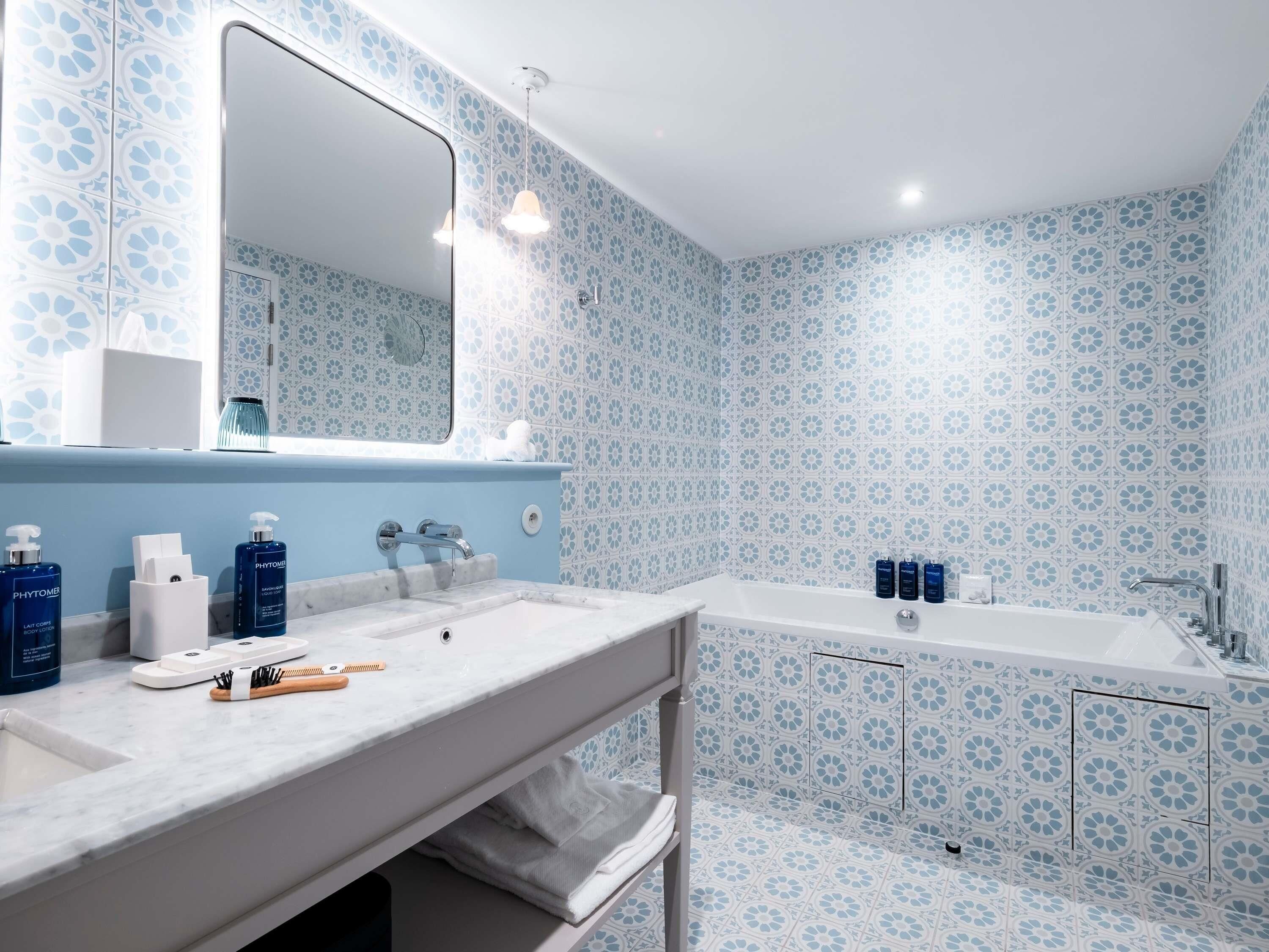 Un baño con un lavamanos blanco, un espejo grande y una bañera. Hay artículos de aseo en la encimera.
