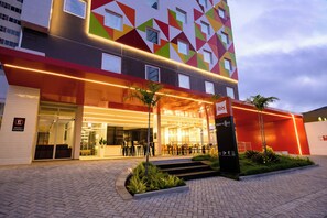 A modern building with a geometric facade, outdoor seating area, and a sign indicating a restaurant. - Ibis Caruaru (Caruaru)