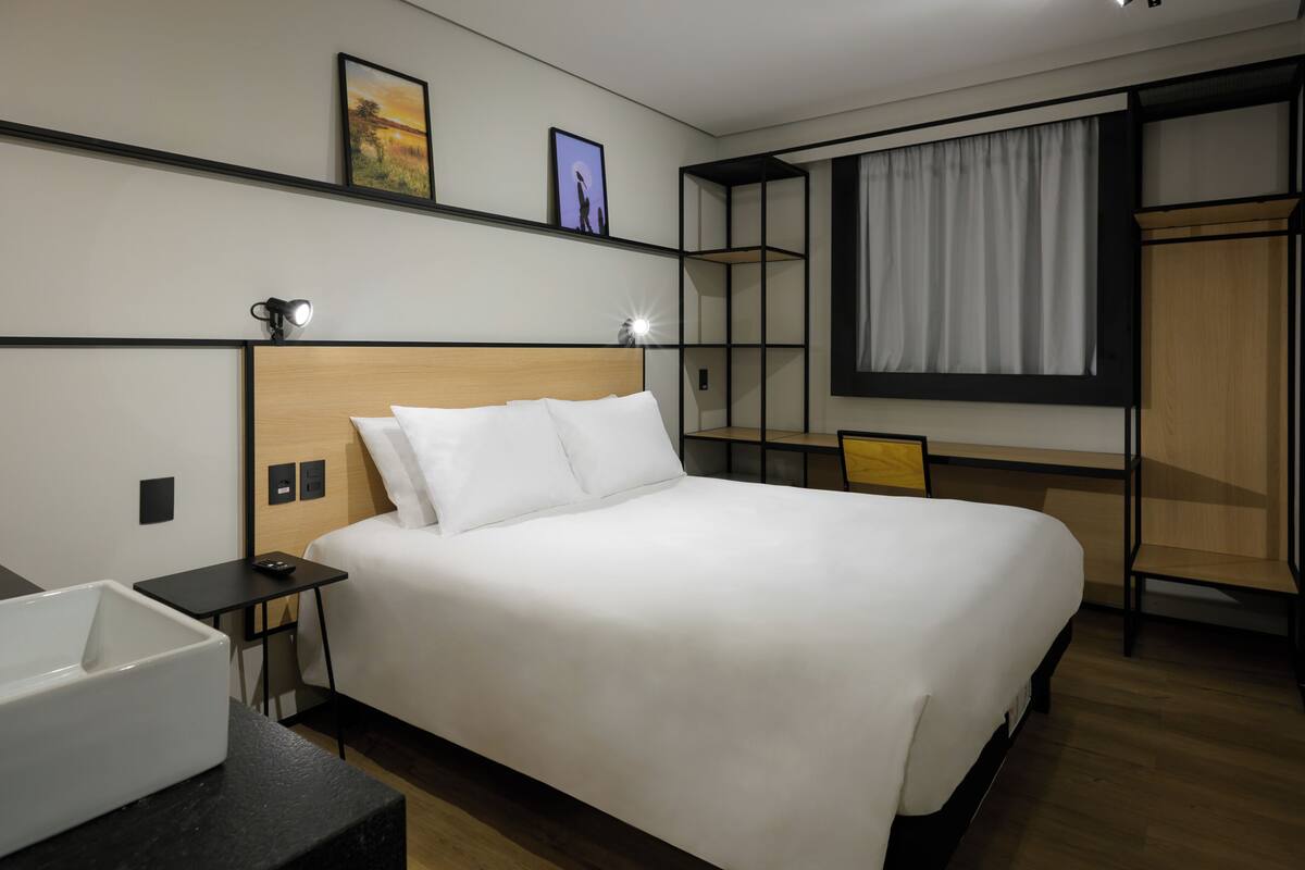 Ein Hotelzimmer mit einem großen Bett, Nachttischen, einem Schreibtisch, einem Stuhl, einem Kleiderschrank und einem Fenster mit Vorhängen.