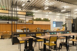 A modern dining area with high tables and chairs, a counter with kitchen appliances, and plants on shelves. - Ibis Caruaru (Caruaru)