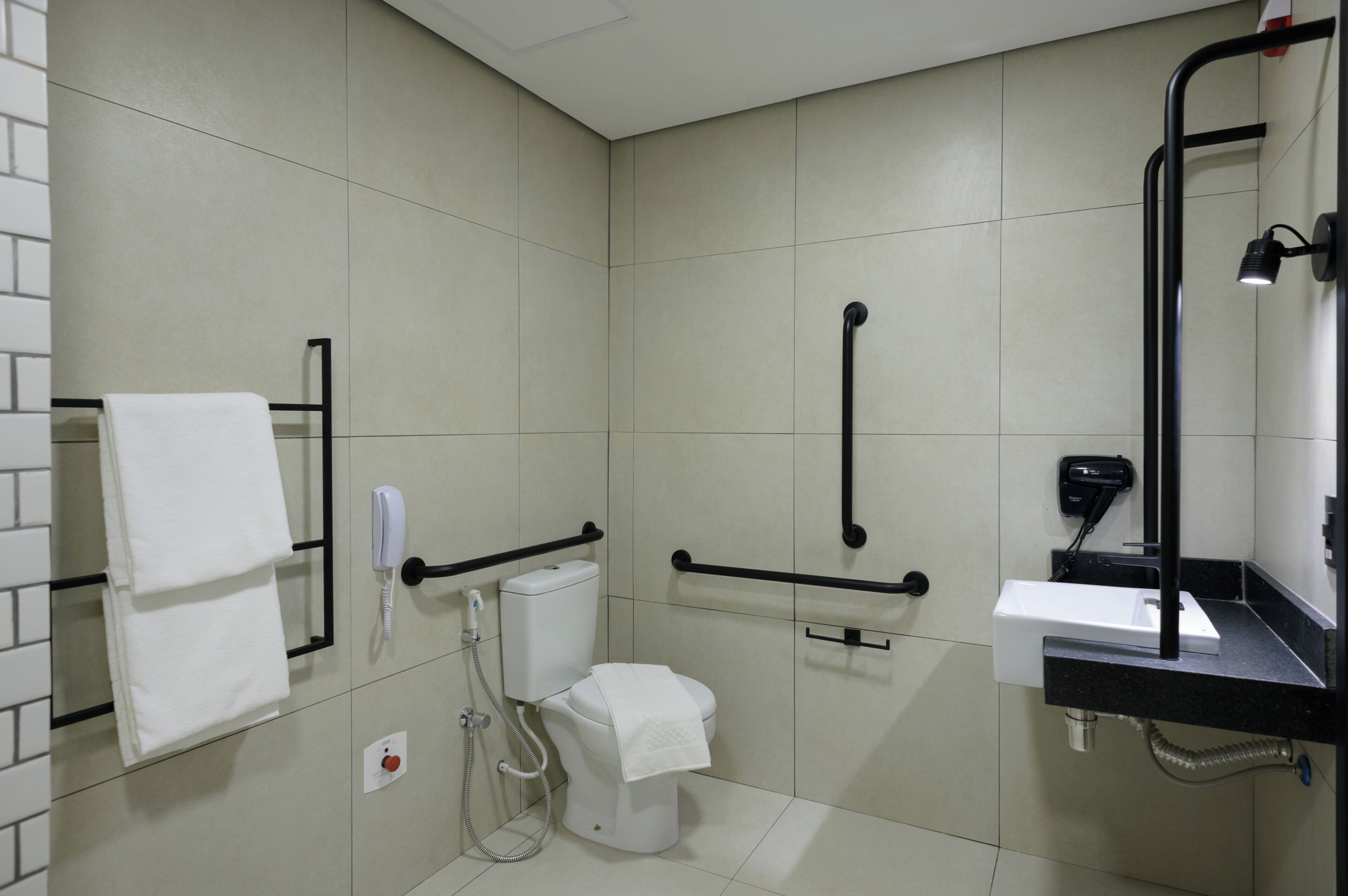 A bathroom with a toilet, handrails, a sink, a mirror, and a towel rack.