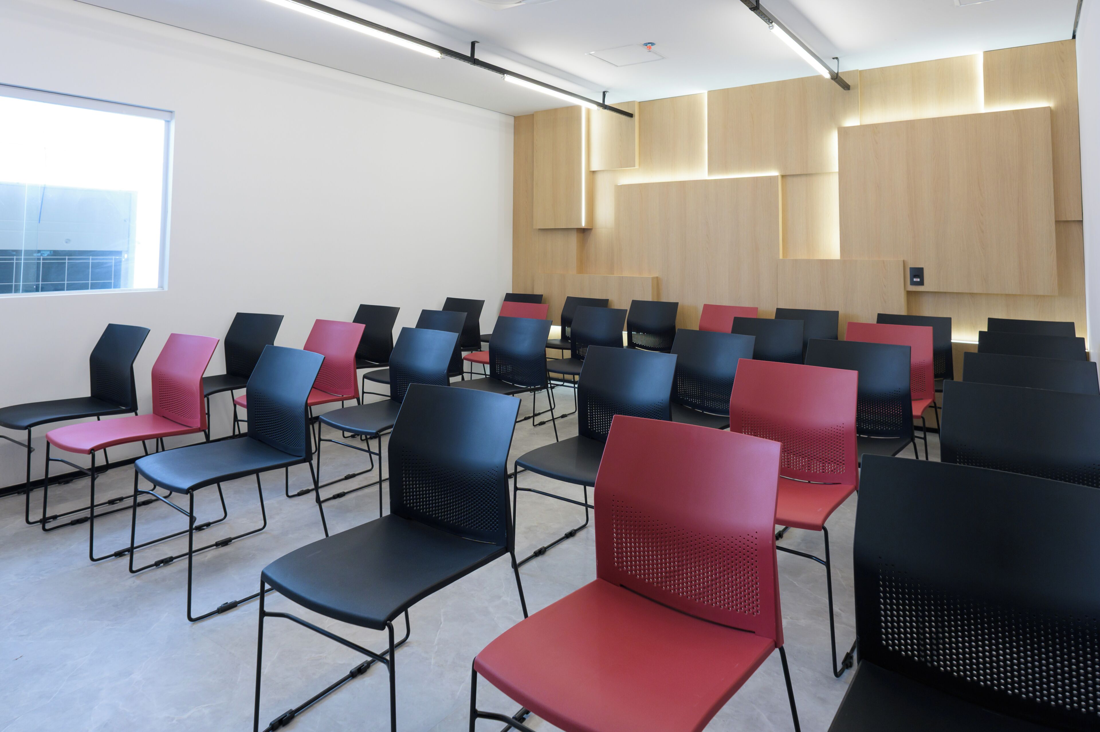 Un salón de conferencias con filas de sillas, un ventanal grande y paneles de madera en las paredes.