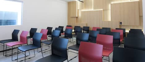 Un salón de conferencias con filas de sillas, un ventanal grande y paneles de madera en las paredes.