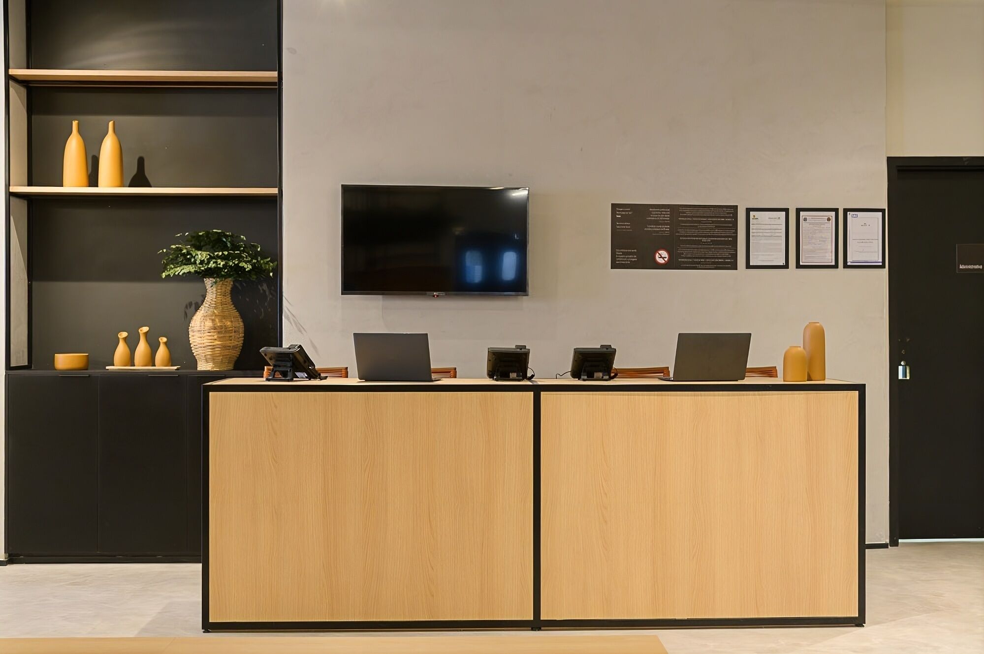 A reception desk with a flat-screen TV, multiple laptops, and a potted plant.