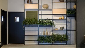 Ein modernes Interieur mit einer dunklen Tür, einem Metallregal mit Pflanzen und verschiedenen Dekorationselementen.