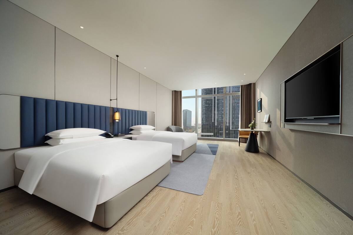 Ein modernes Hotelzimmer mit zwei Betten, einem großen Fernseher und Blick auf die Stadt.