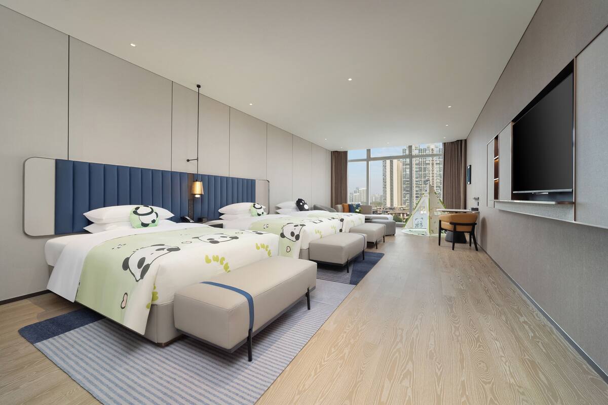 Ein modernes Hotelzimmer mit einem großen Bett, einer Couch, einem Fernseher und Blick auf die Stadt.
