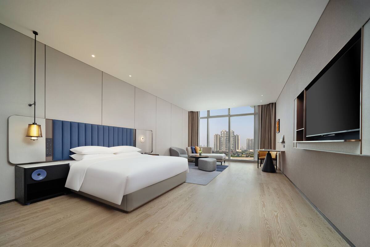 Ein modernes Hotelzimmer mit einem großen Bett, einem Fernseher, einem Schreibtisch und Blick auf die Stadt.