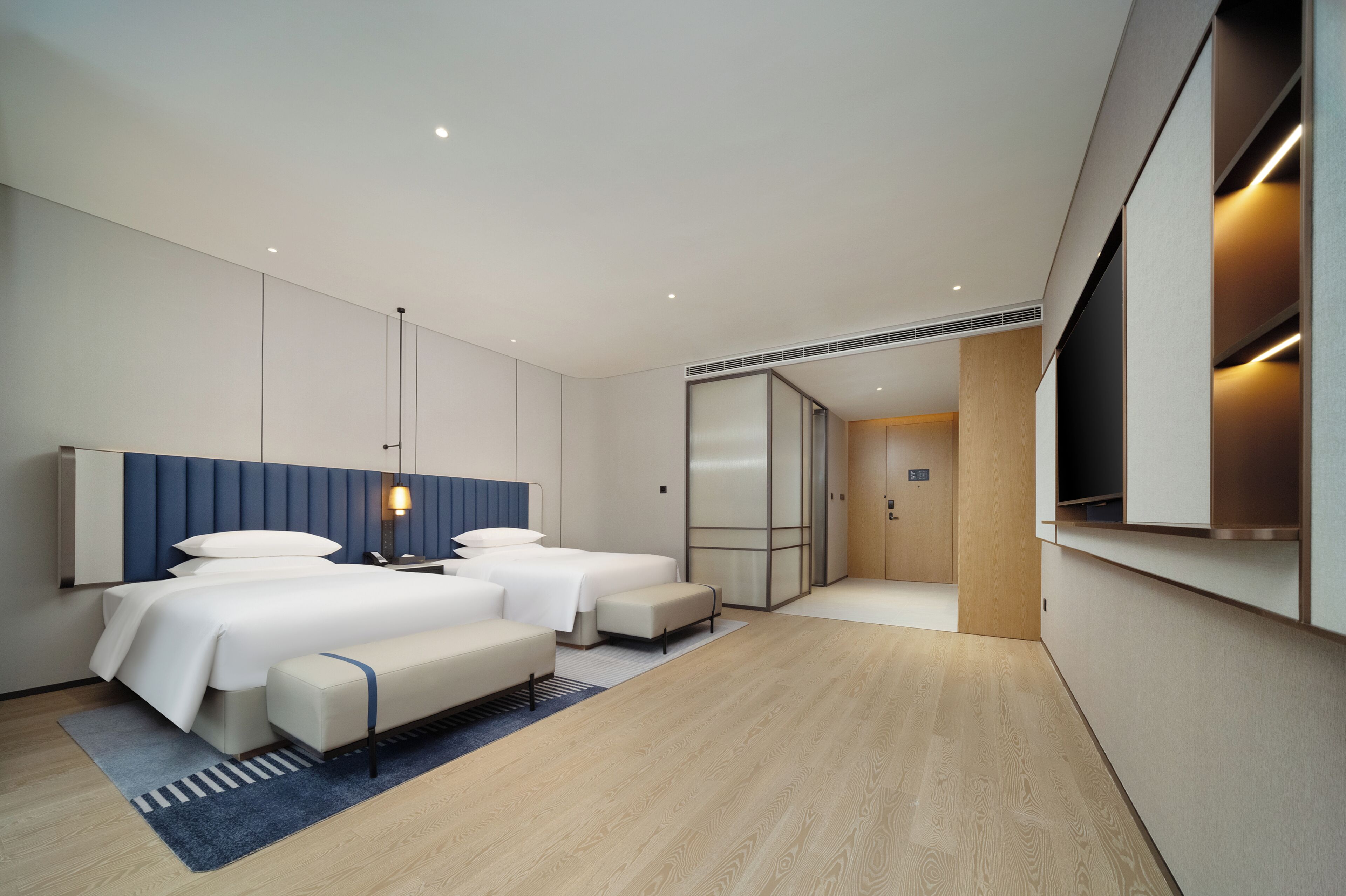 A modern hotel room with a large bed, two bedside tables, a desk, and a wardrobe.