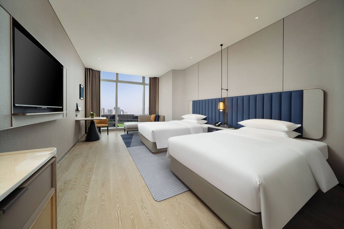 Ein modernes Hotelzimmer mit zwei Betten, einem Flachbildfernseher, einem Schreibtisch und Blick auf die Stadt.