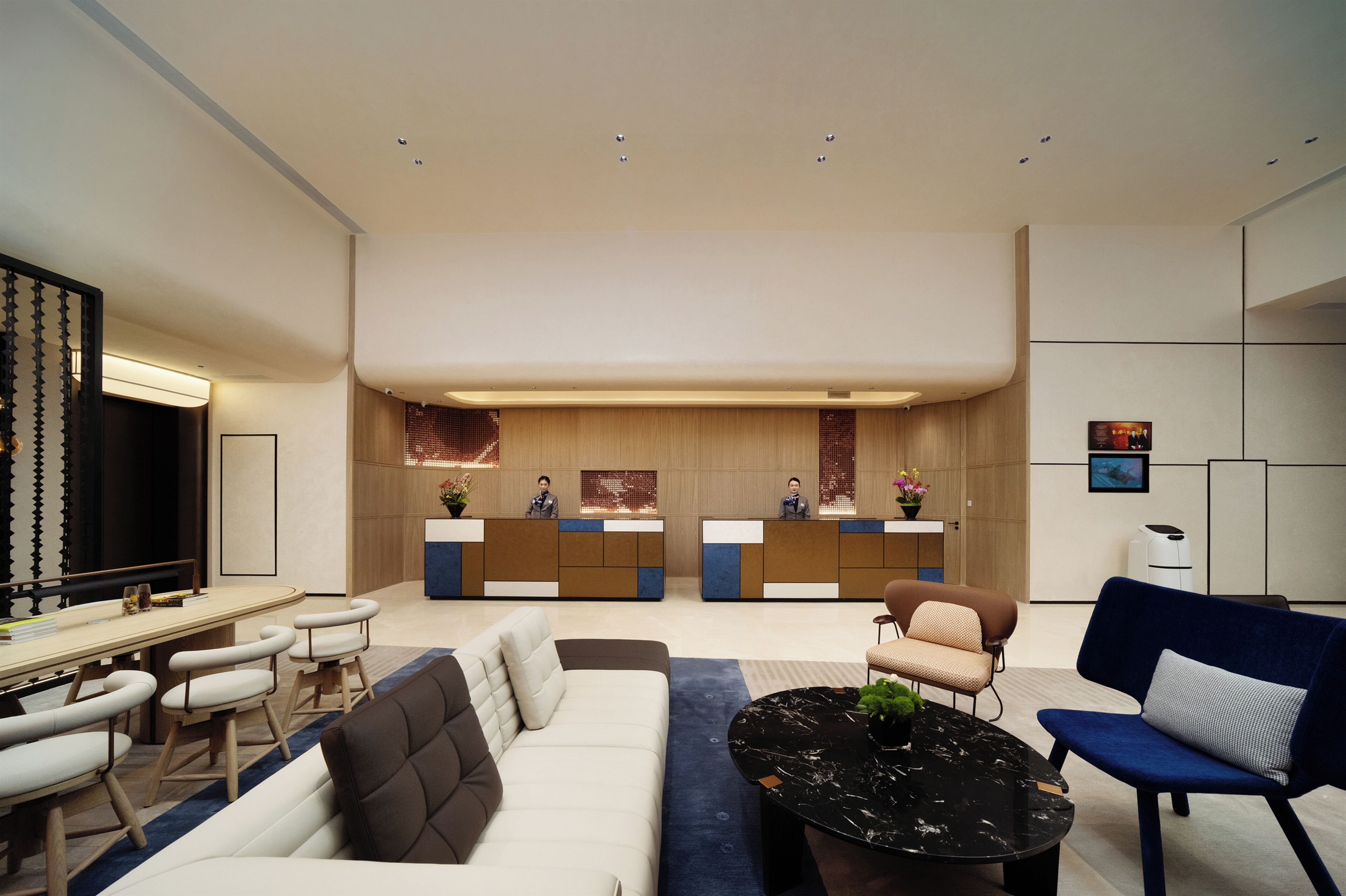 A modern hotel lobby with a reception desk, seating area, and a television.