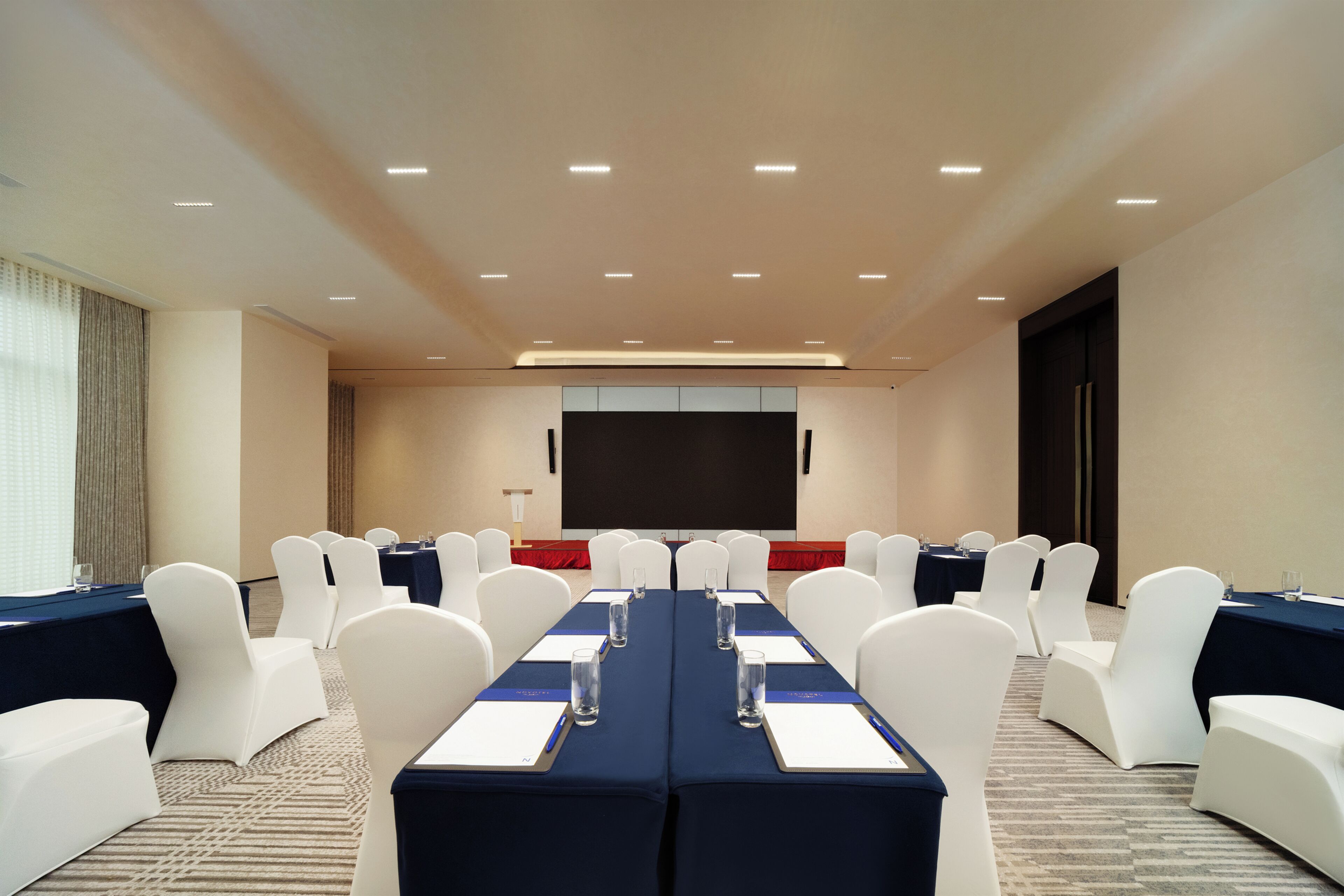 Un salón de conferencias con una larga mesa, sillas blancas y una pantalla para proyector.