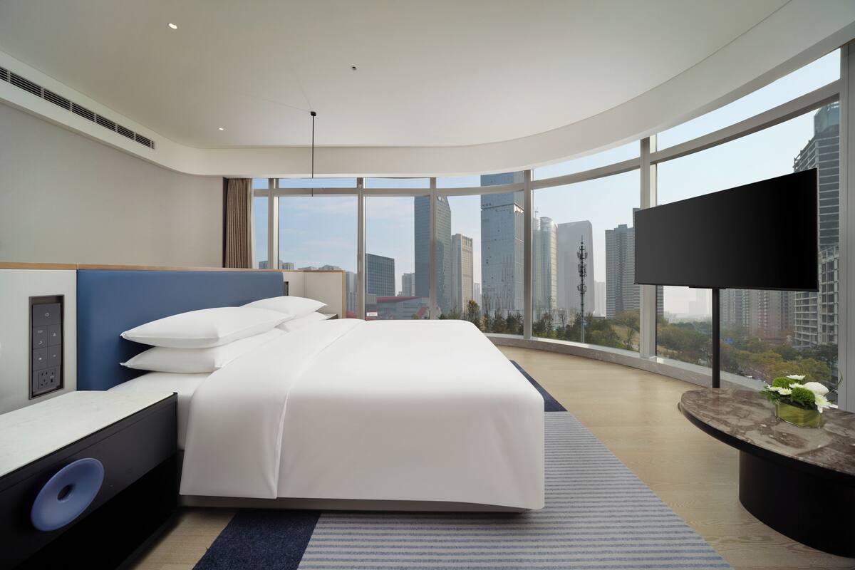 Ein modernes Hotelzimmer mit einem großen Bett, einem Flachbildfernseher und Blick auf die Stadt.