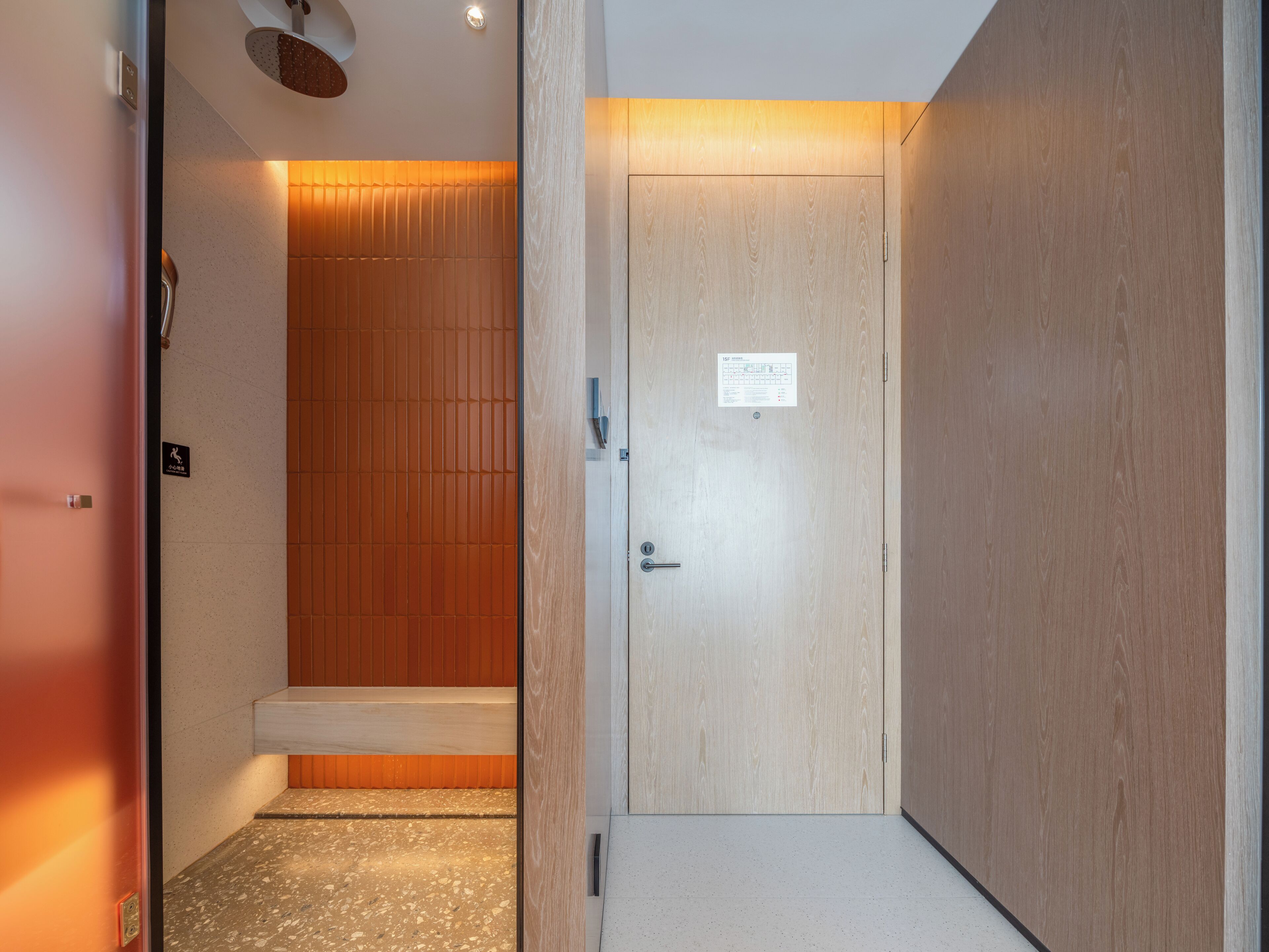 A hallway with a wooden door, a shower area, and a tiled floor.