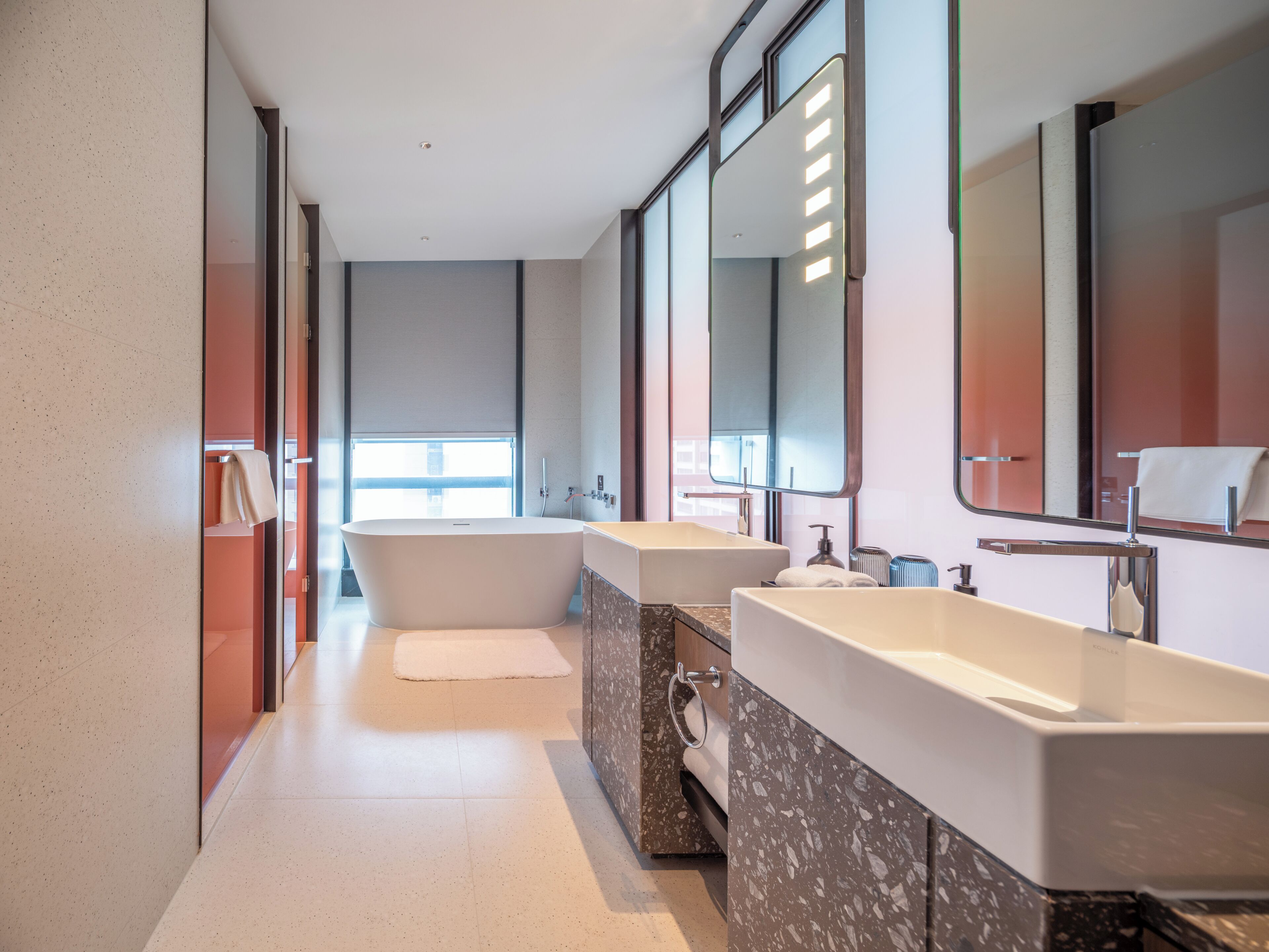 A modern bathroom with a freestanding bathtub, two sinks, and large mirrors.