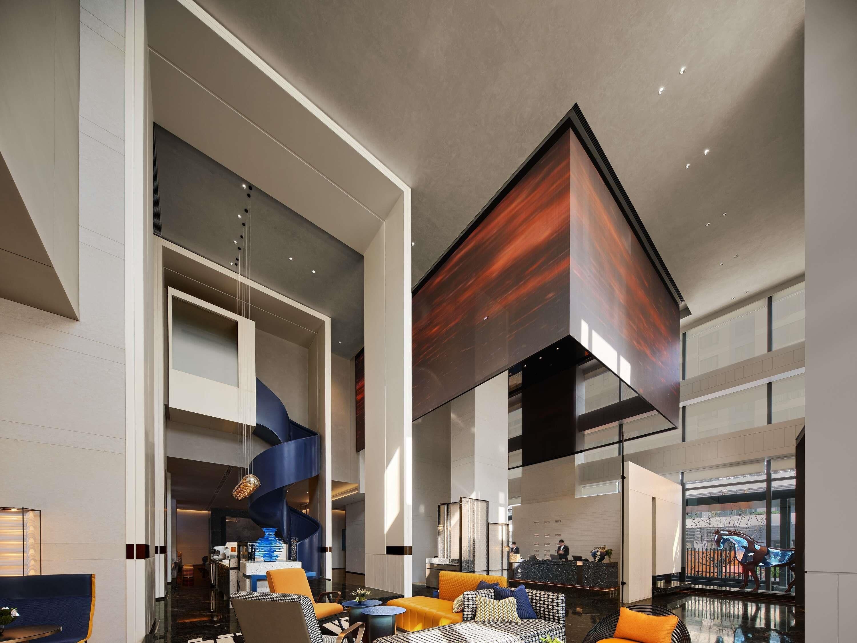 A modern hotel lobby with a high ceiling, a spiral staircase, and a reception desk.