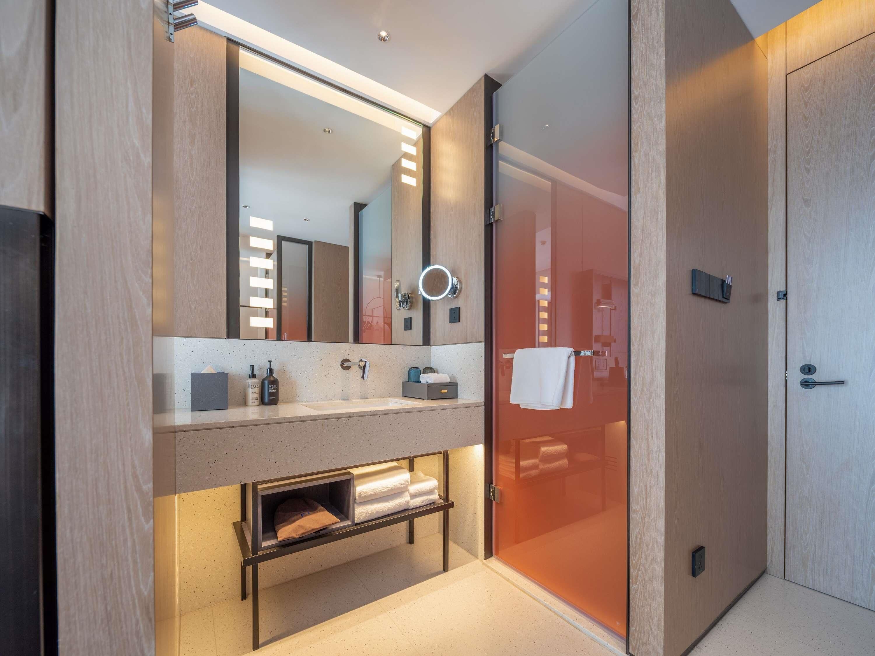 Une salle de bain moderne avec un grand miroir, un meuble-lavabo, un porte-serviettes et une cabine de douche en verre.