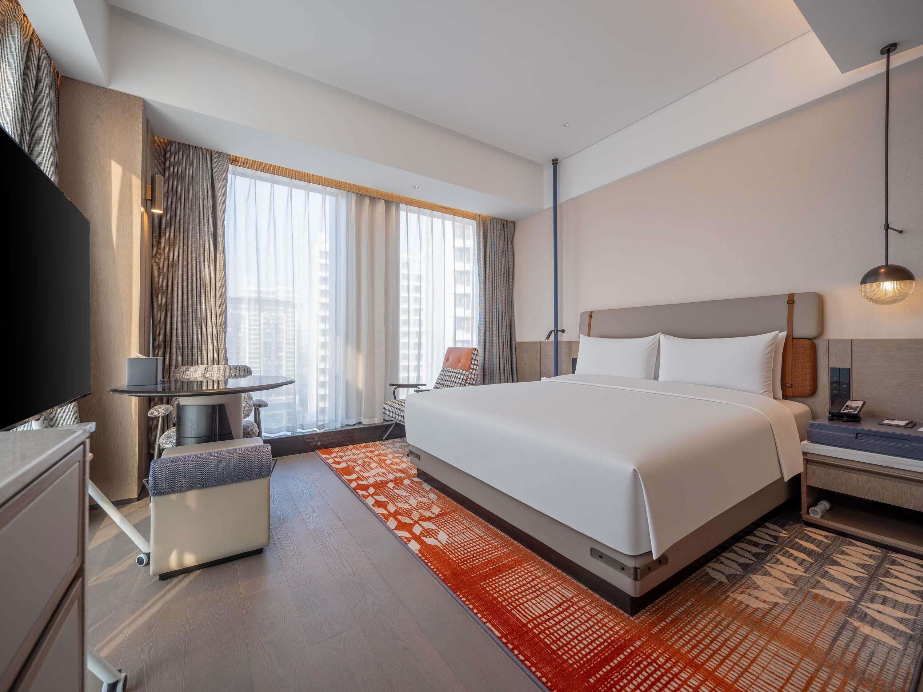 A hotel room with a bed, a desk, a chair, a TV, and a window with curtains.