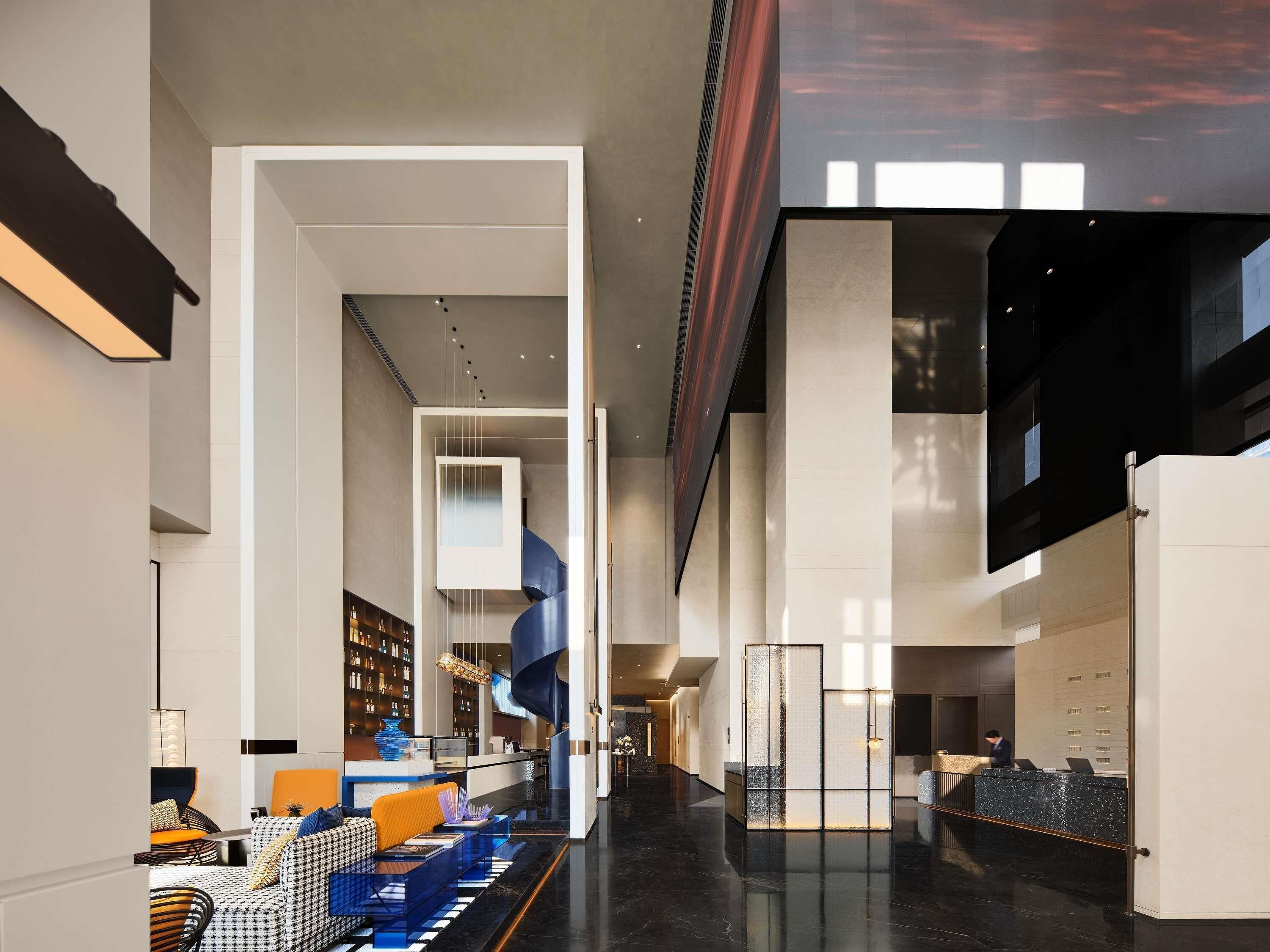 A modern lobby with a central staircase, seating areas, and a reception desk.