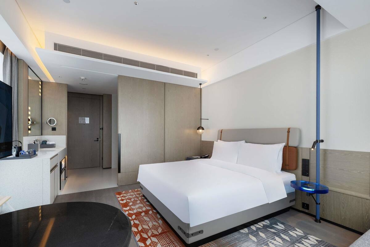 Una habitación de hotel moderna con una cama grande, un escritorio, una silla, un espejo y un baño.
