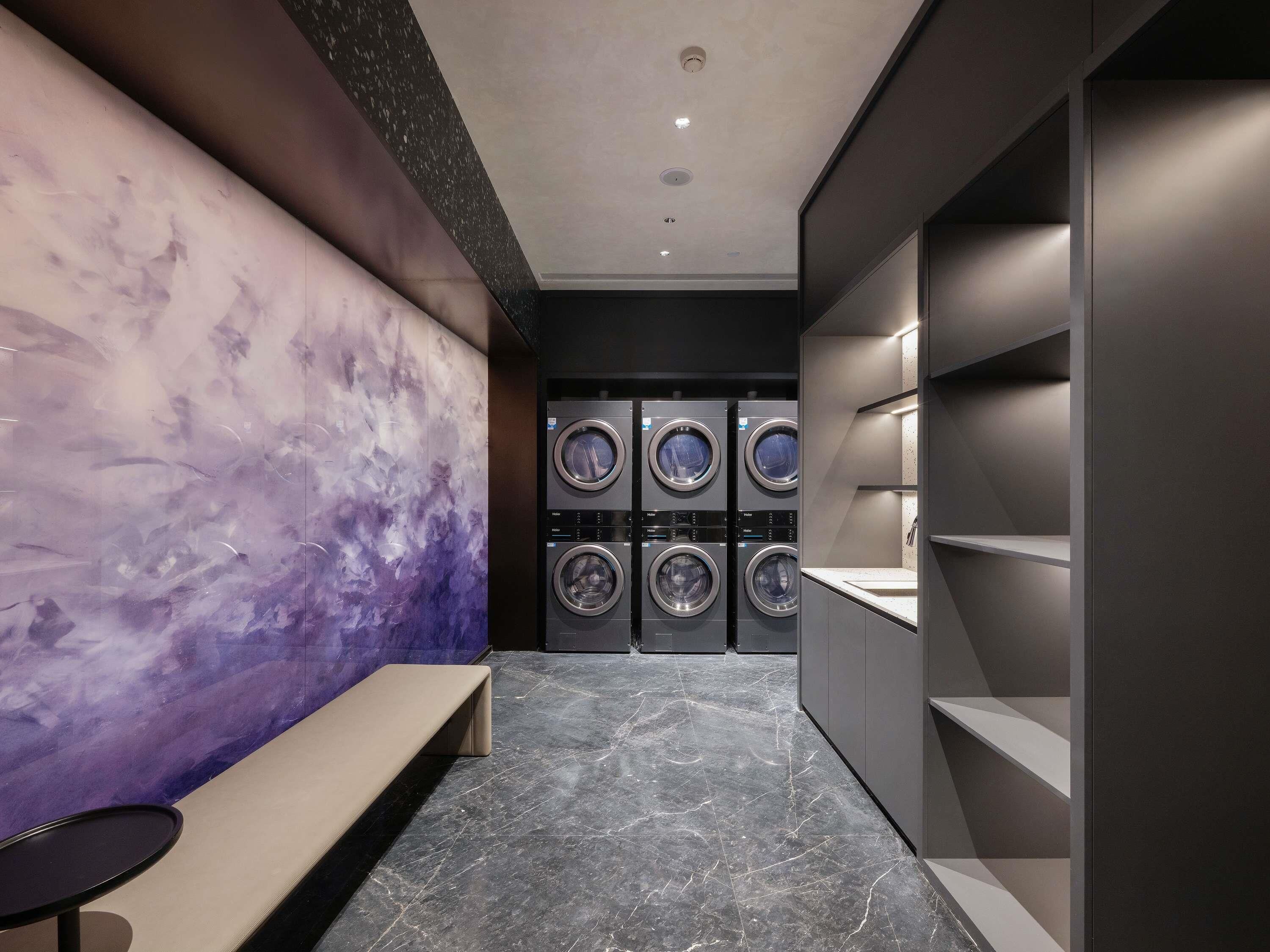 A modern laundry room with a marble wall, a bench, and a row of washing machines.