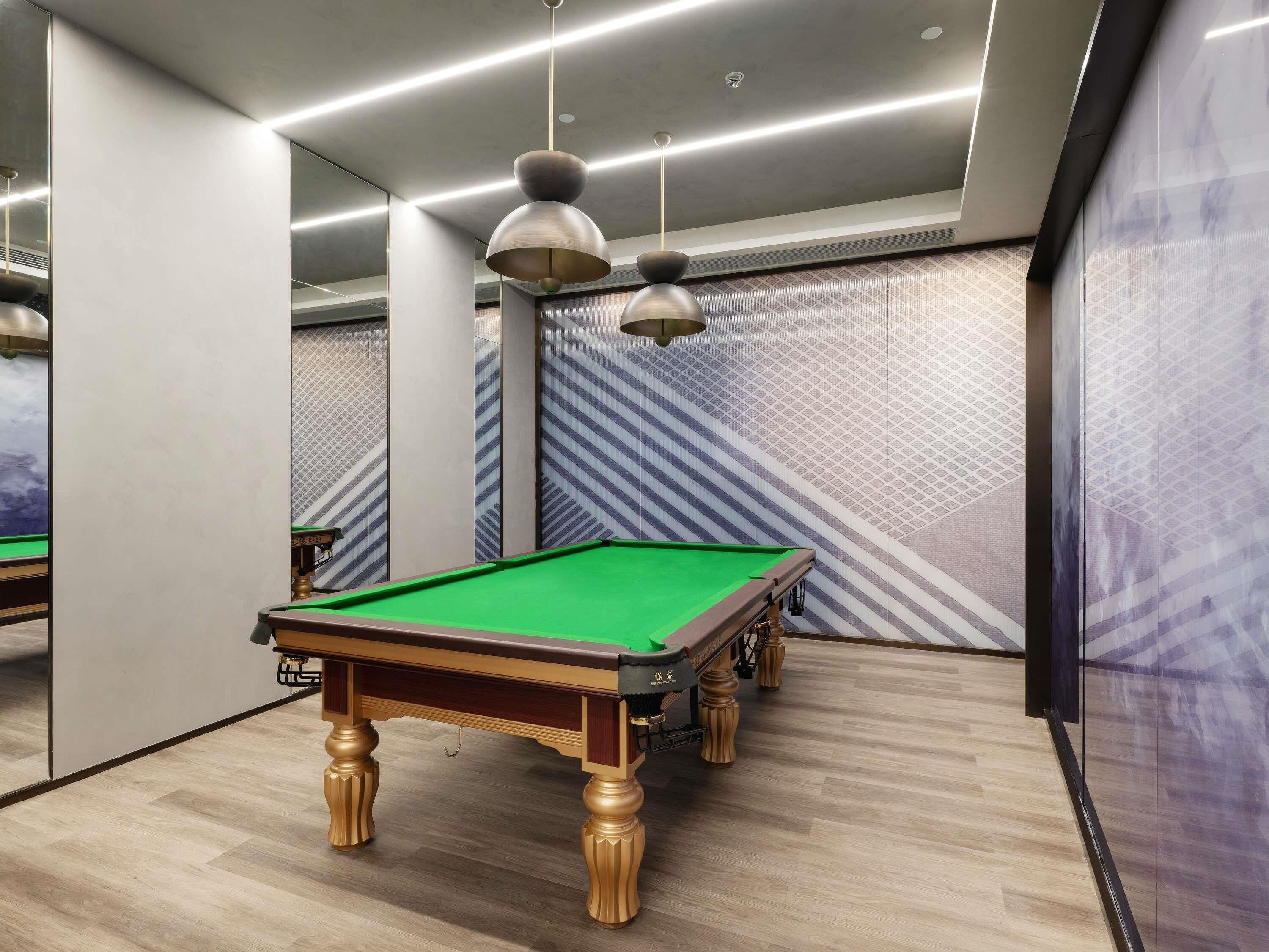 Una mesa de billar con superficie de fieltro verde, patas de madera y un espejo con un diseño geométrico.