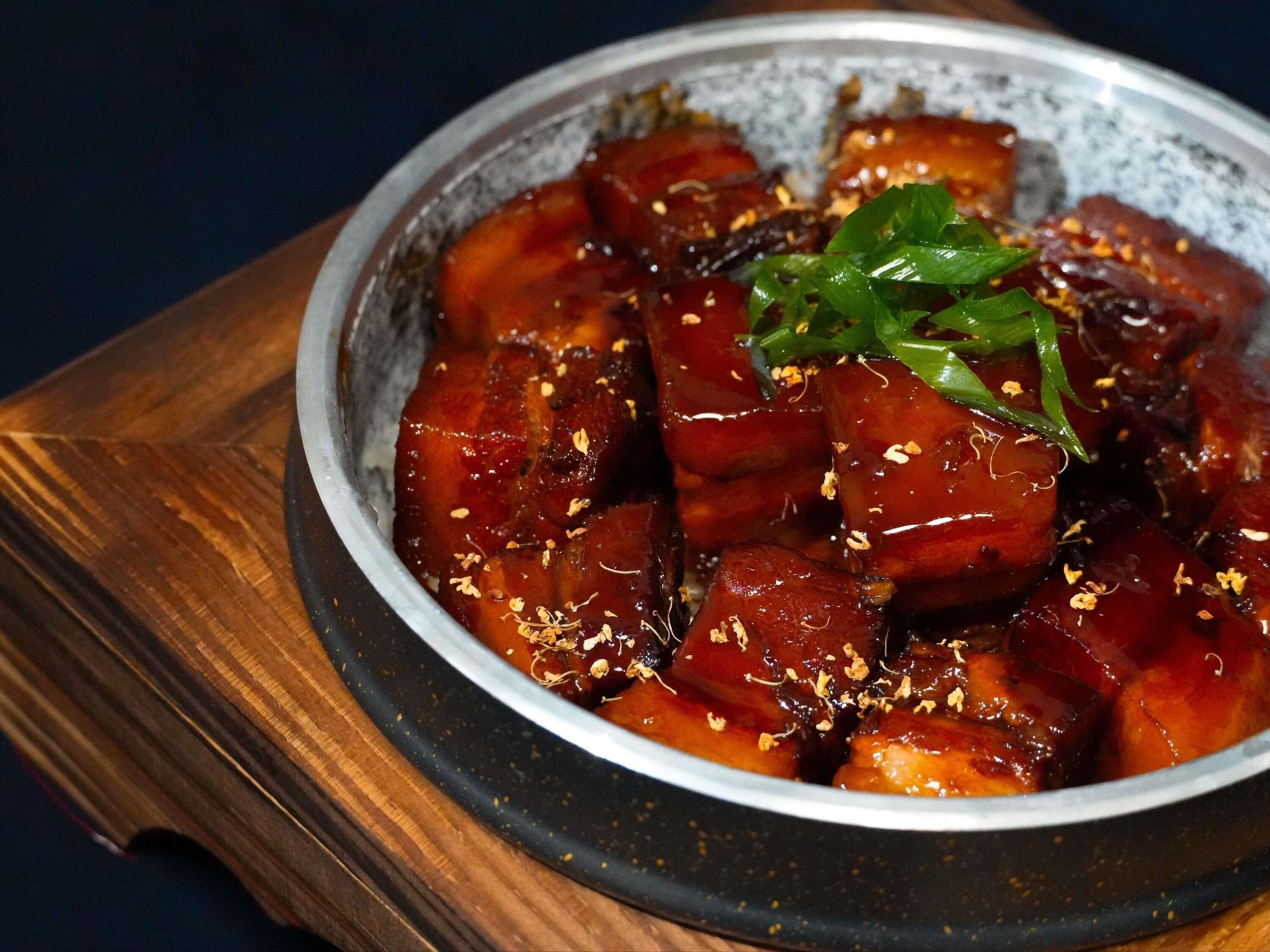 A bowl of glazed meat with garnish on a wooden board.