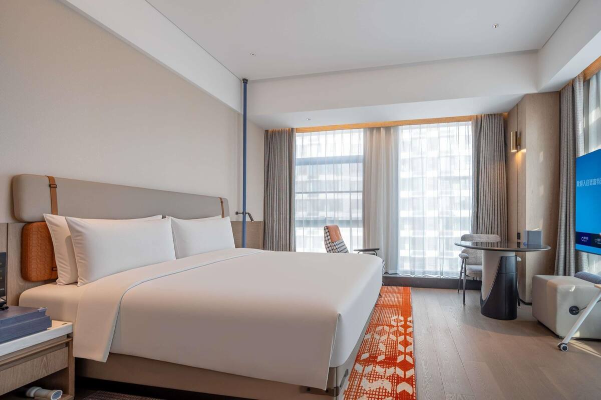 Habitación de hotel con cama, escritorio, silla, televisor y ventana con cortinas.