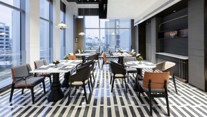 Un espace de restauration moderne, doté de tables et de chaises, de grandes fenêtres et offrant une vue sur la ville.