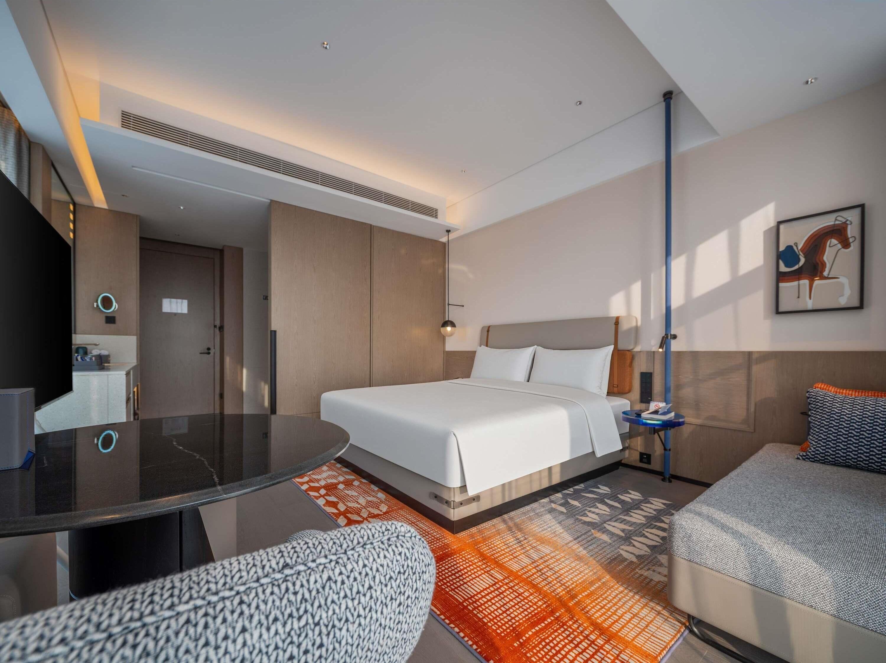 A modern hotel room with a bed, a desk, a sofa, and a bathroom.