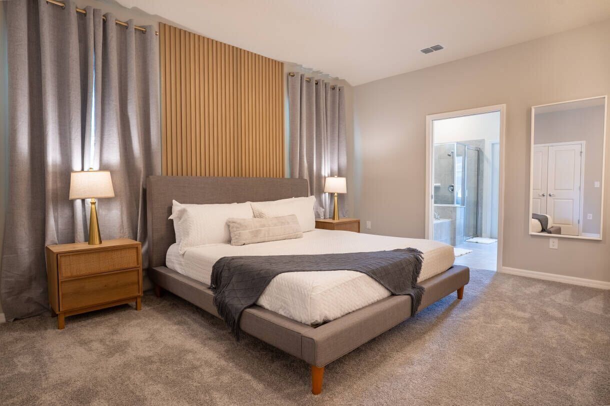 Een moderne slaapkamer met een groot bed, twee nachtkastjes en een spiegel aan de muur.