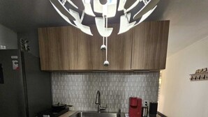 Une cuisine compacte dotée de meubles en bois, d’un évier en acier inoxydable et d’un luminaire suspendu moderne.