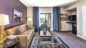 Ein Hotelzimmer mit einer Couch, einem Sessel, einem Couchtisch, einem Fernseher und Blick ins Freie.