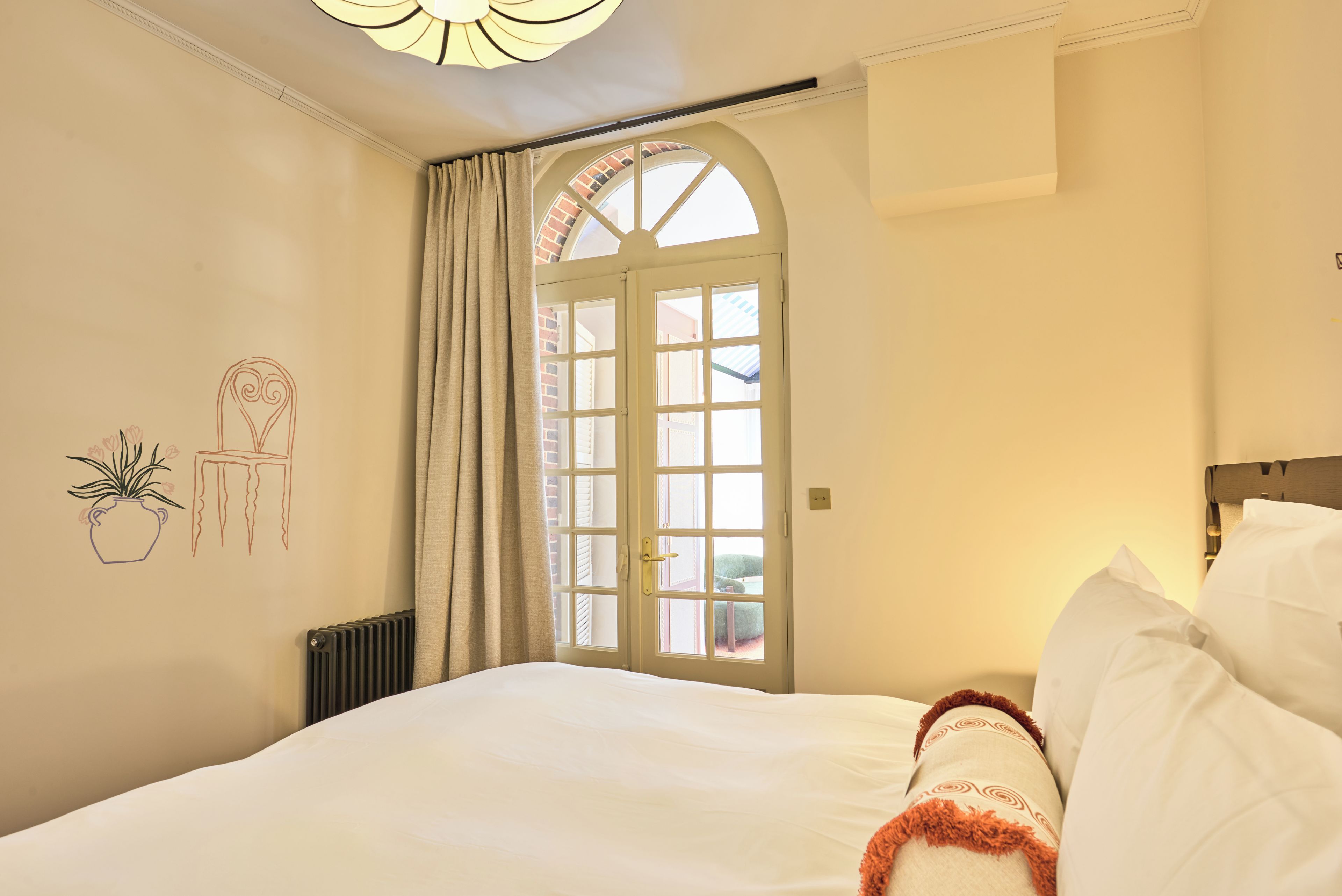 Un dormitorio con cama, una ventana con cortinas, un radiador y decoración en la pared.