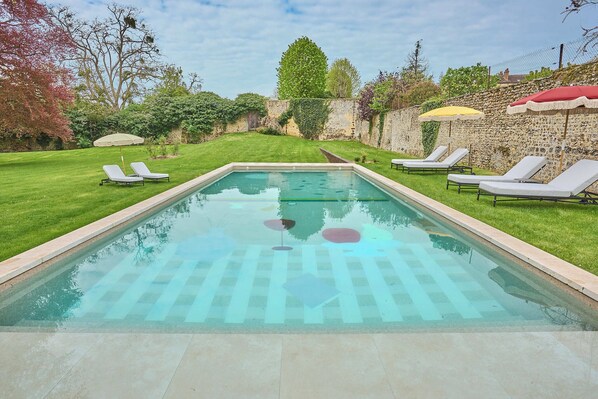A rectangular swimming pool with a checkered pattern, surrounded by a stone wall, with lounge chairs and umbrellas. - Verneuil la douce (Verneuil d'Avre et d'Iton)
