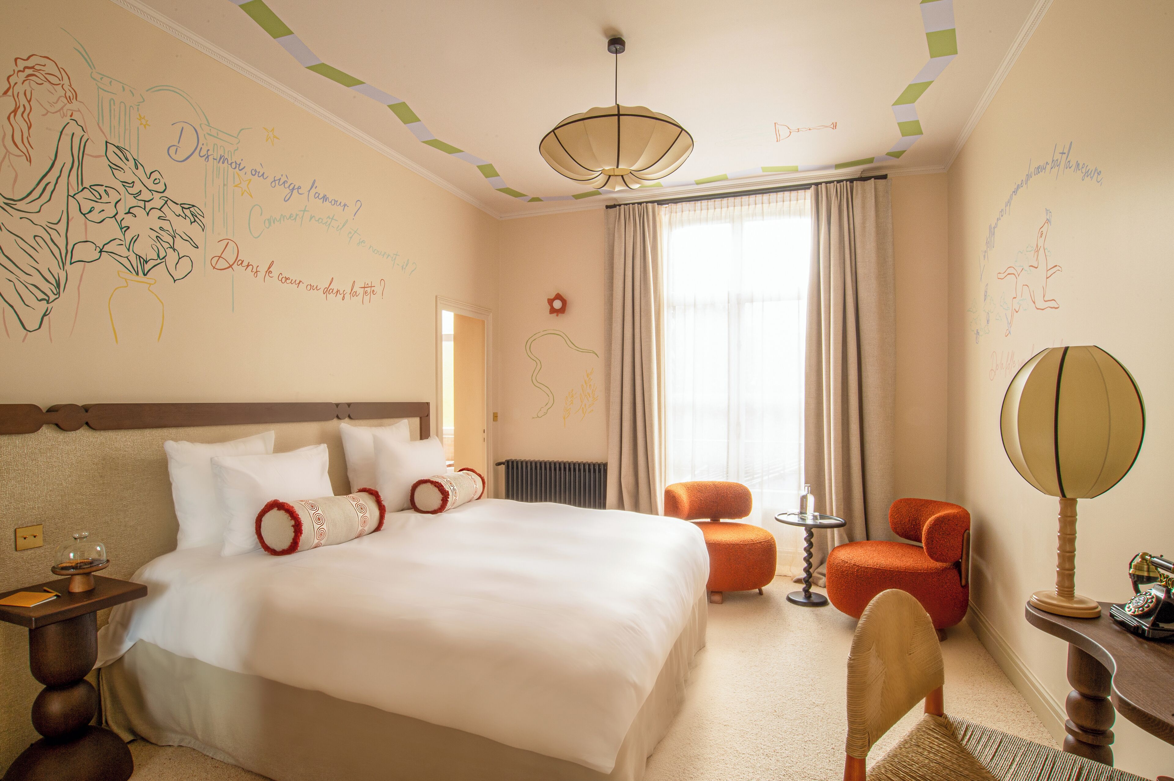 A hotel room with a large bed, a chair, a small table, a lamp, and a window with curtains.