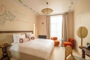 Habitación de hotel con una cama grande, una silla, una mesita, una lámpara y un ventanal con cortinas.