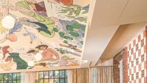 Una sala de estar acogedora con un gran mural, asientos cómodos, una chimenea y ventanas amplias.