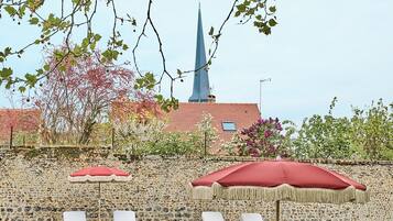 A patio area with lounge chairs and umbrellas, a stone wall, and a building with a spire in the background.