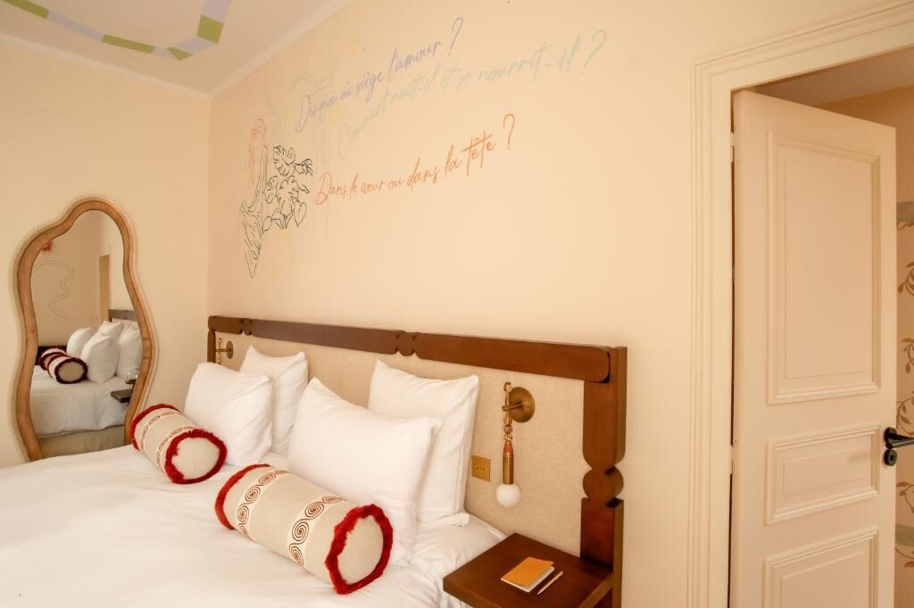 Een hotelkamer met een bed, nachtkastje, spiegel en een muur met decoratieve tekst.