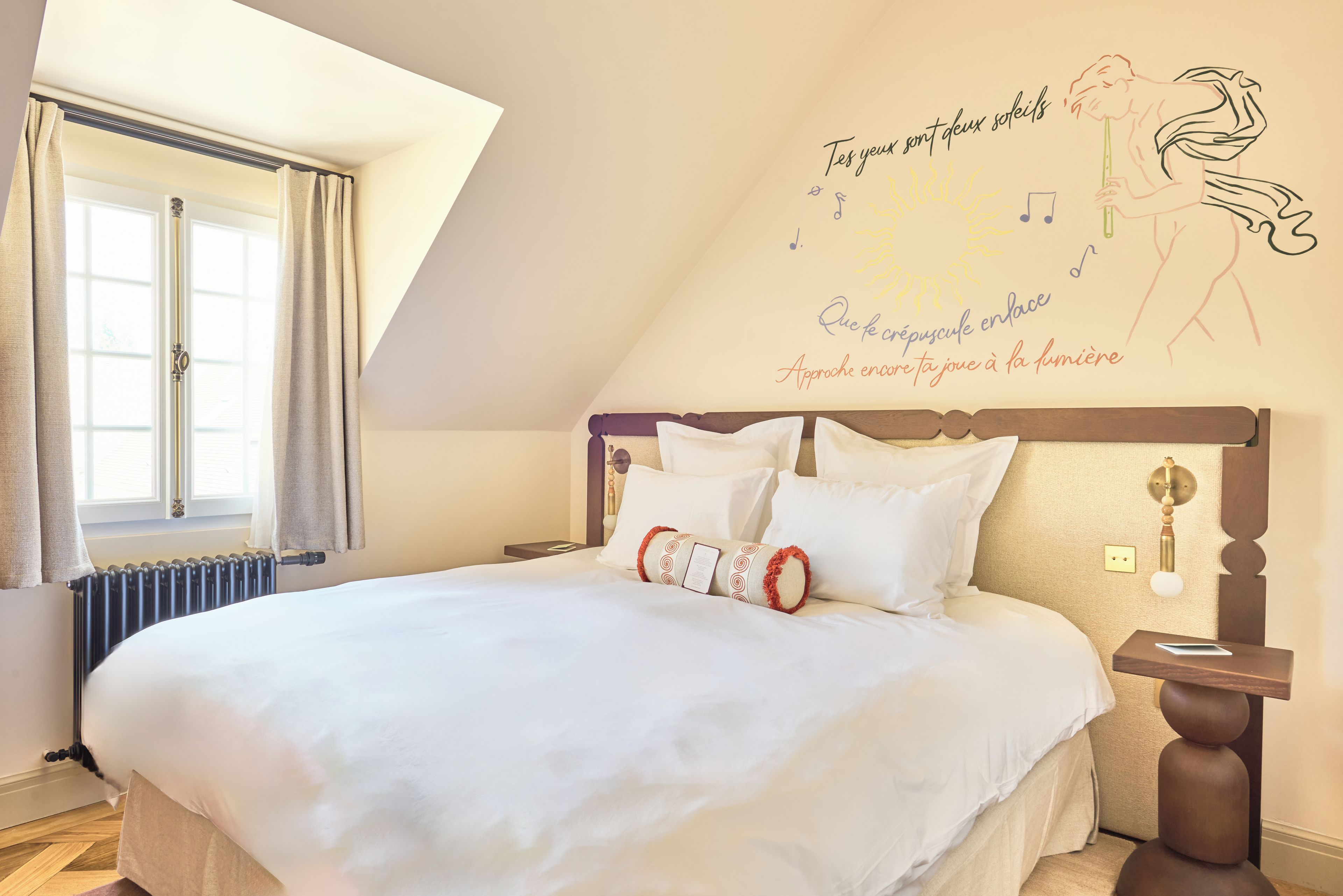 Une chambre à coucher avec un grand lit, une fenêtre avec des rideaux, un radiateur et un mur orné d’un motif décoratif.